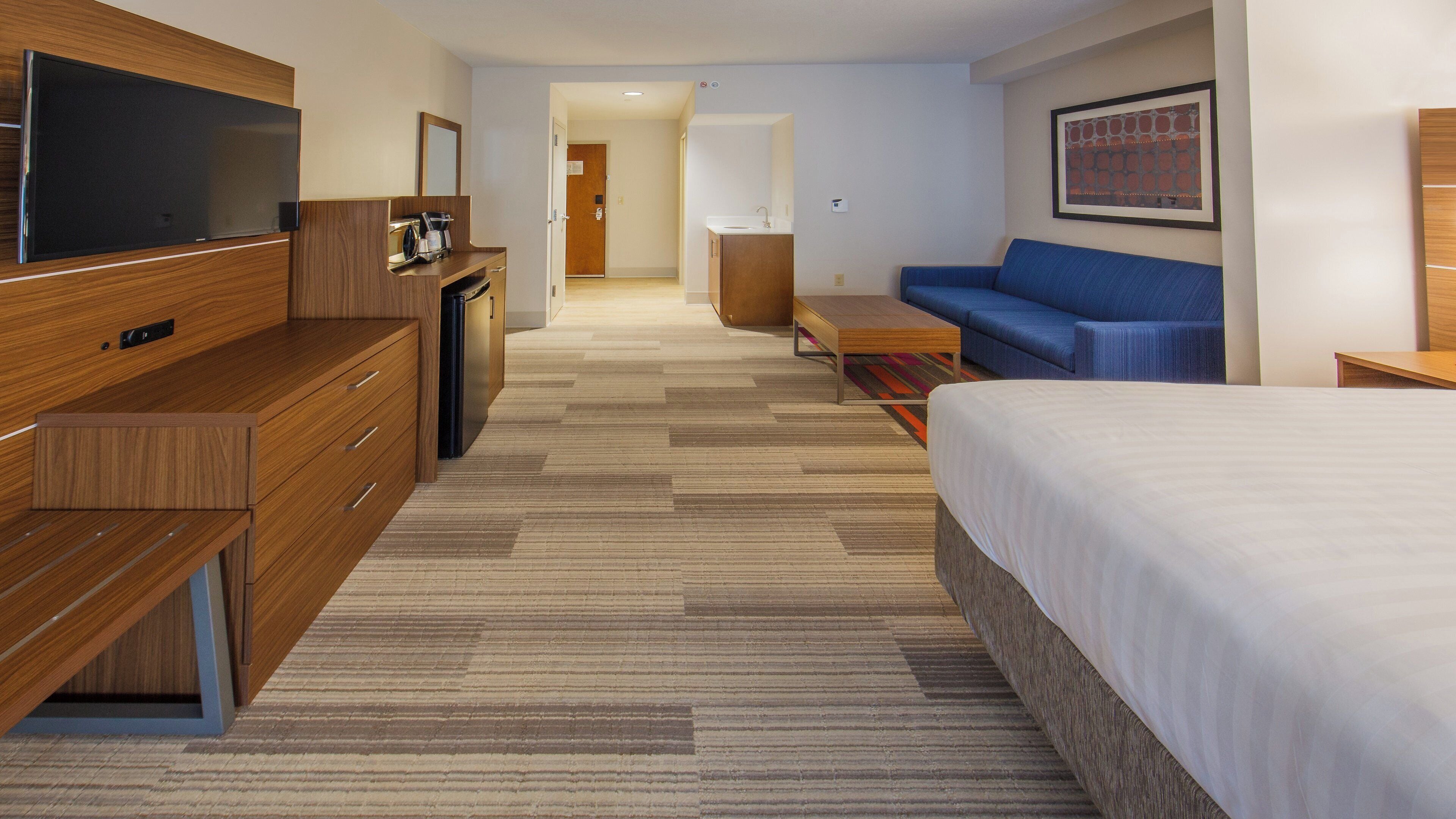 Une chambre d’hôtel comprenant un lit, un canapé, un bureau avec une télévision à écran plat, une machine à café et une salle de bain avec un lavabo et un miroir.