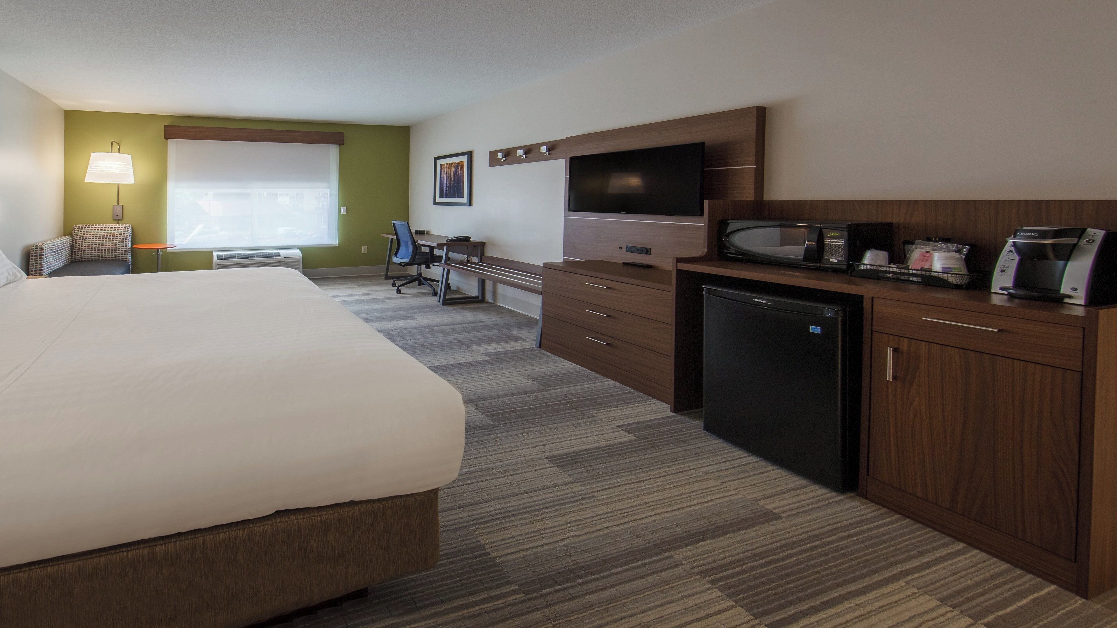 A hotel room with a bed, desk, kitchenette, and a television.