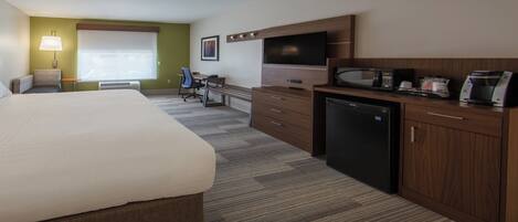 A hotel room with a bed, desk, kitchenette, and a television.