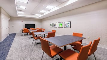 A conference room with tables and chairs, a flat-screen TV, and framed pictures on the wall.