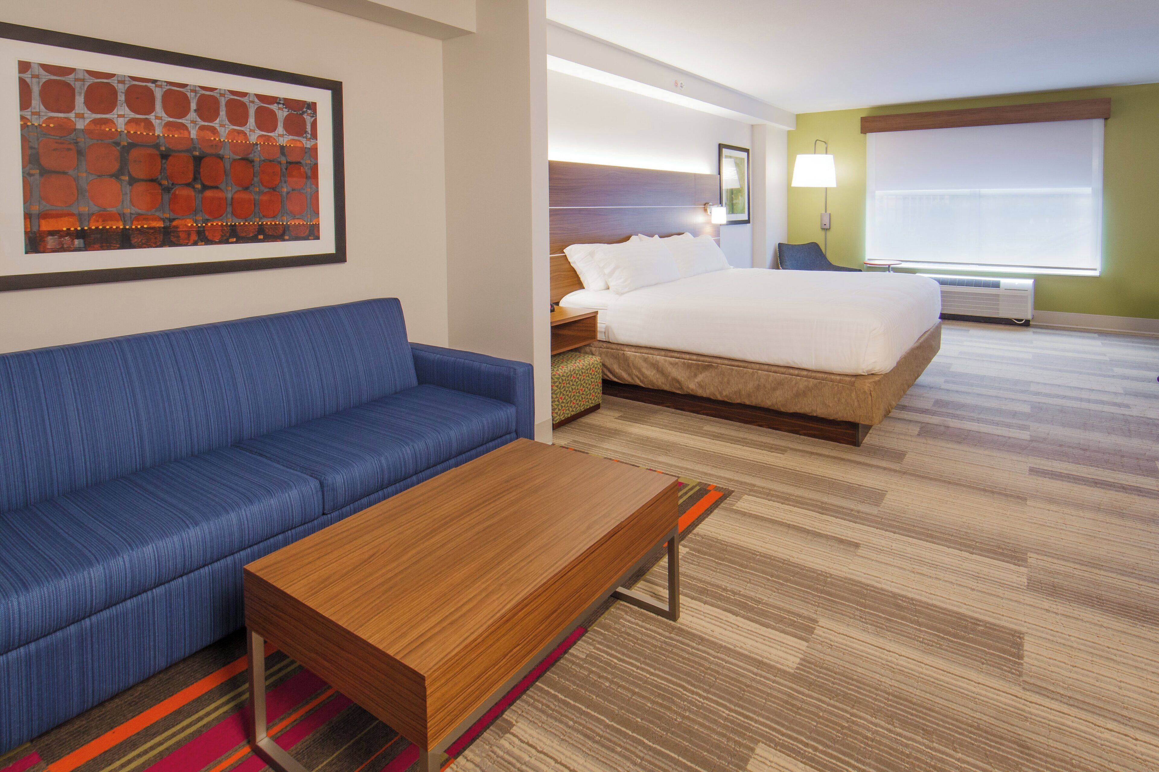 A hotel room with a bed, a blue sofa, a wooden coffee table, and a colorful rug.