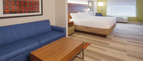 A hotel room with a bed, a blue sofa, a wooden coffee table, and a colorful rug.