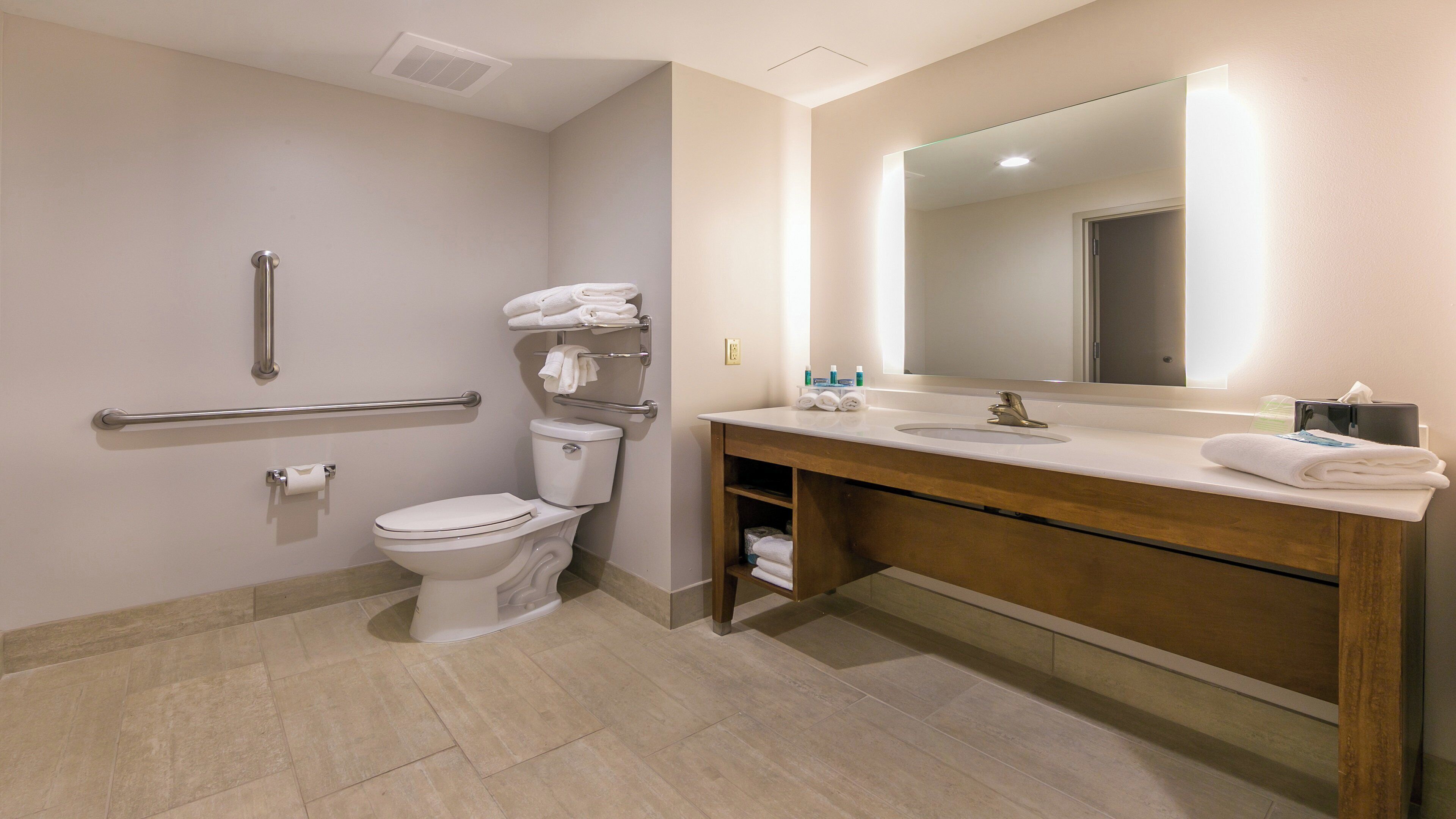 A modern bathroom with a toilet, handrails, a sink with a mirror, and neatly folded towels.