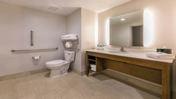 A modern bathroom with a toilet, handrails, a sink with a mirror, and neatly folded towels.