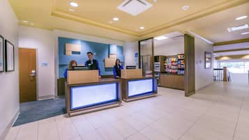 A hotel reception area with a modern design, featuring a reception desk, a self-service kiosk, and a counter with snacks.
