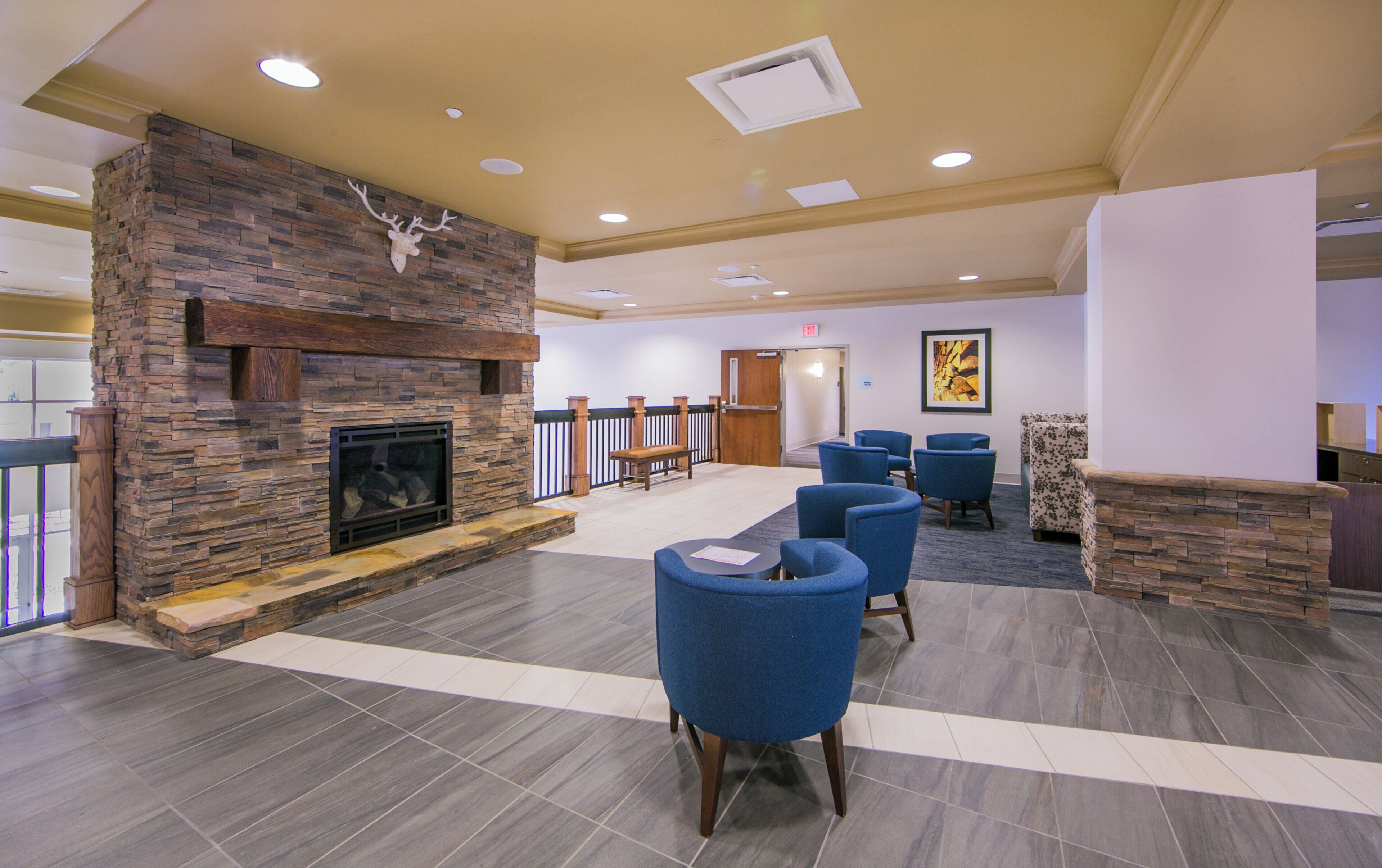 A lobby with a stone fireplace, blue chairs, and a wooden bench.
