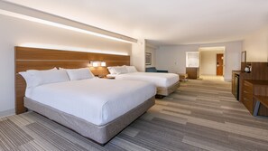 Quarto de hotel com duas camas, uma escrivaninha, uma cadeira, mesa de cabeceira, luminária e banheiro com pia e espelho.