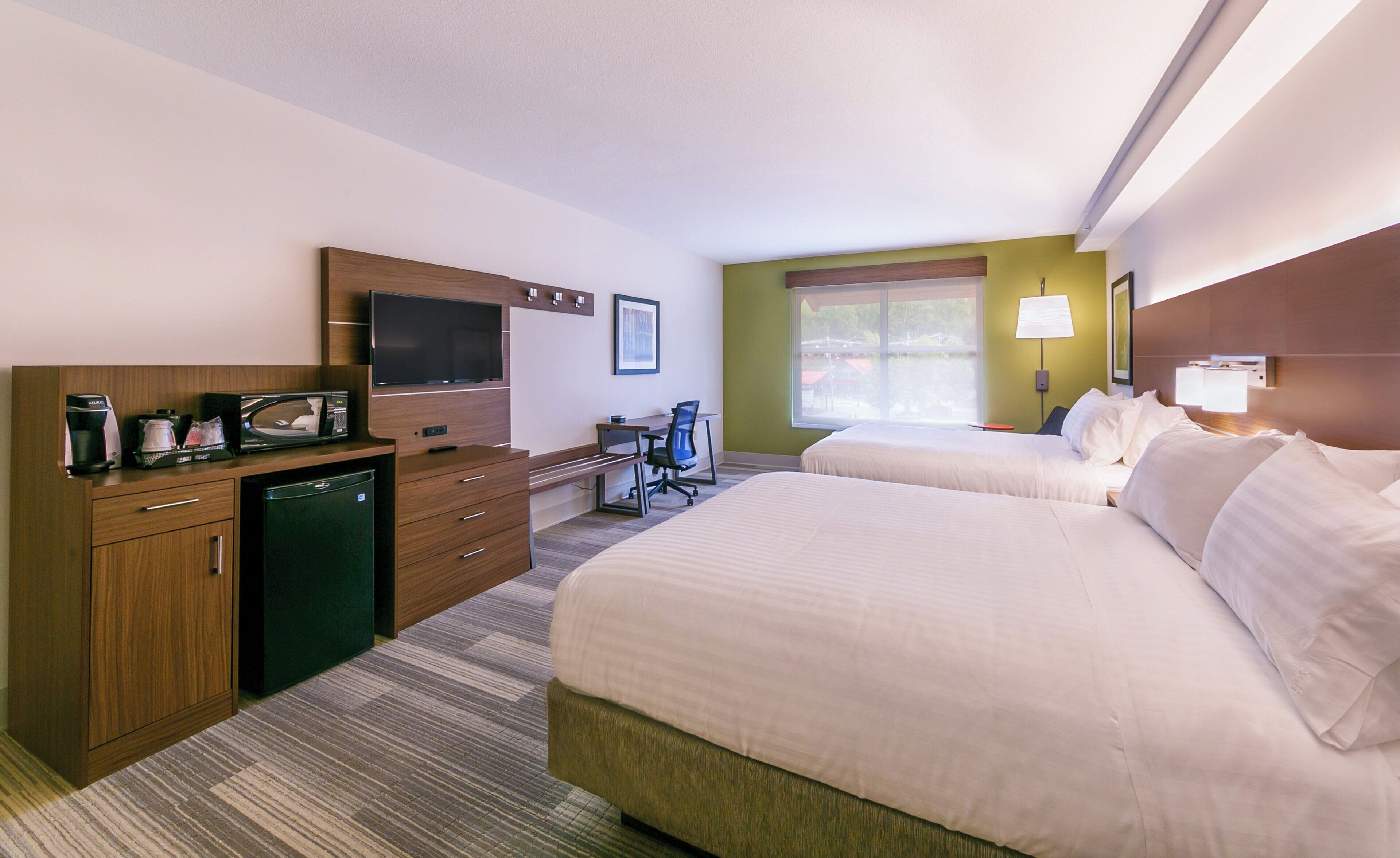 A hotel room with two beds, a desk with a chair, a television, a coffee maker, and a window with a view.