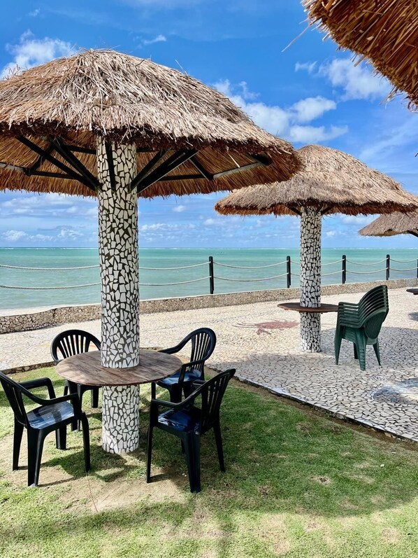 Un espace de détente aménagé sur la plage, avec des parasols en chaume, une table recouverte de mosaïques et des chaises.