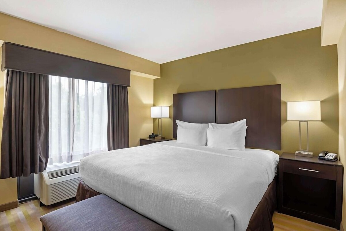 Habitación de hotel con una cama grande, lámparas de noche, una mesita de noche con un teléfono y una ventana con cortinas.