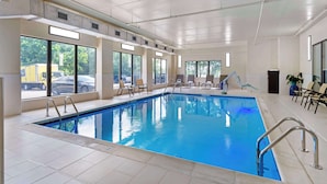 Uma piscina interior com janelas amplas, chão revestido de azulejos e algumas cadeiras de descanso.