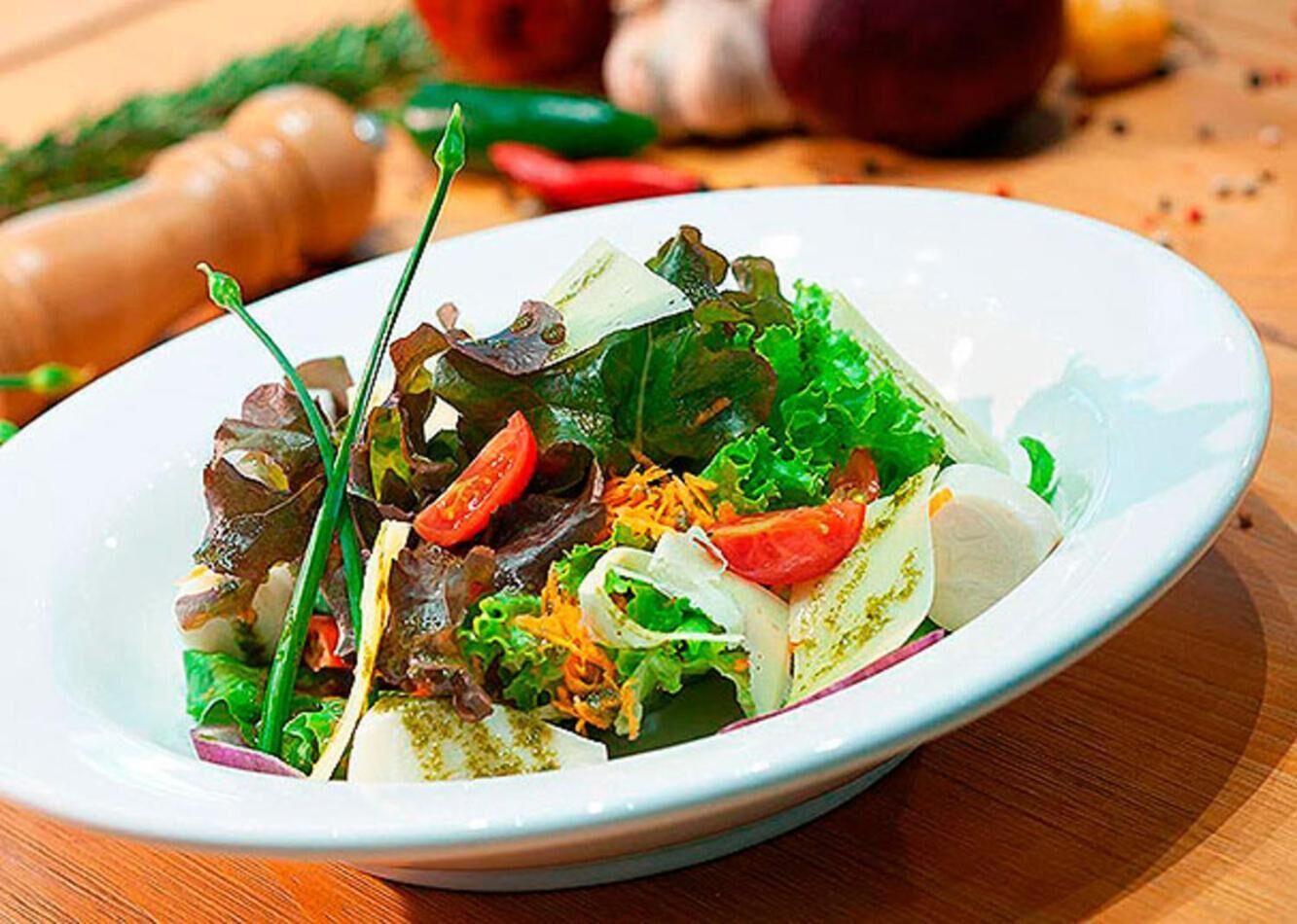 A plate of mixed greens salad with various vegetables and herbs.