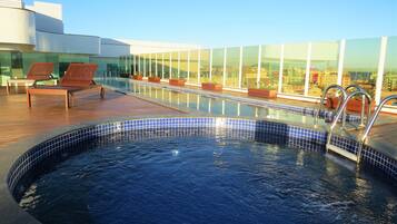 Una piscina en la azotea con sillones de descanso, un jacuzzi y una terraza acristalada con vistas a la ciudad.