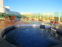 Una piscina en la azotea con sillones de descanso, un jacuzzi y una terraza acristalada con vistas a la ciudad.