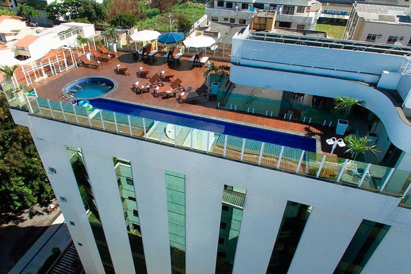 A rooftop pool area with lounge chairs and umbrellas, surrounded by a high-rise building with large windows.