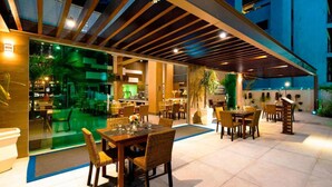 An outdoor dining area with tables and chairs, a pool, and a covered seating area. - Oásis Cabo Frio Hotel (Cabo Frio)