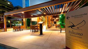 Uma área externa de restaurante com mesas, cadeiras e um espaço coberto para sentar, além de uma placa com o nome do restaurante.