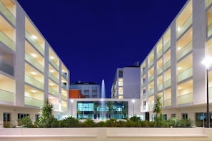 Um hotel moderno com um pátio central, guarda-corpos de vidro e uma fonte.