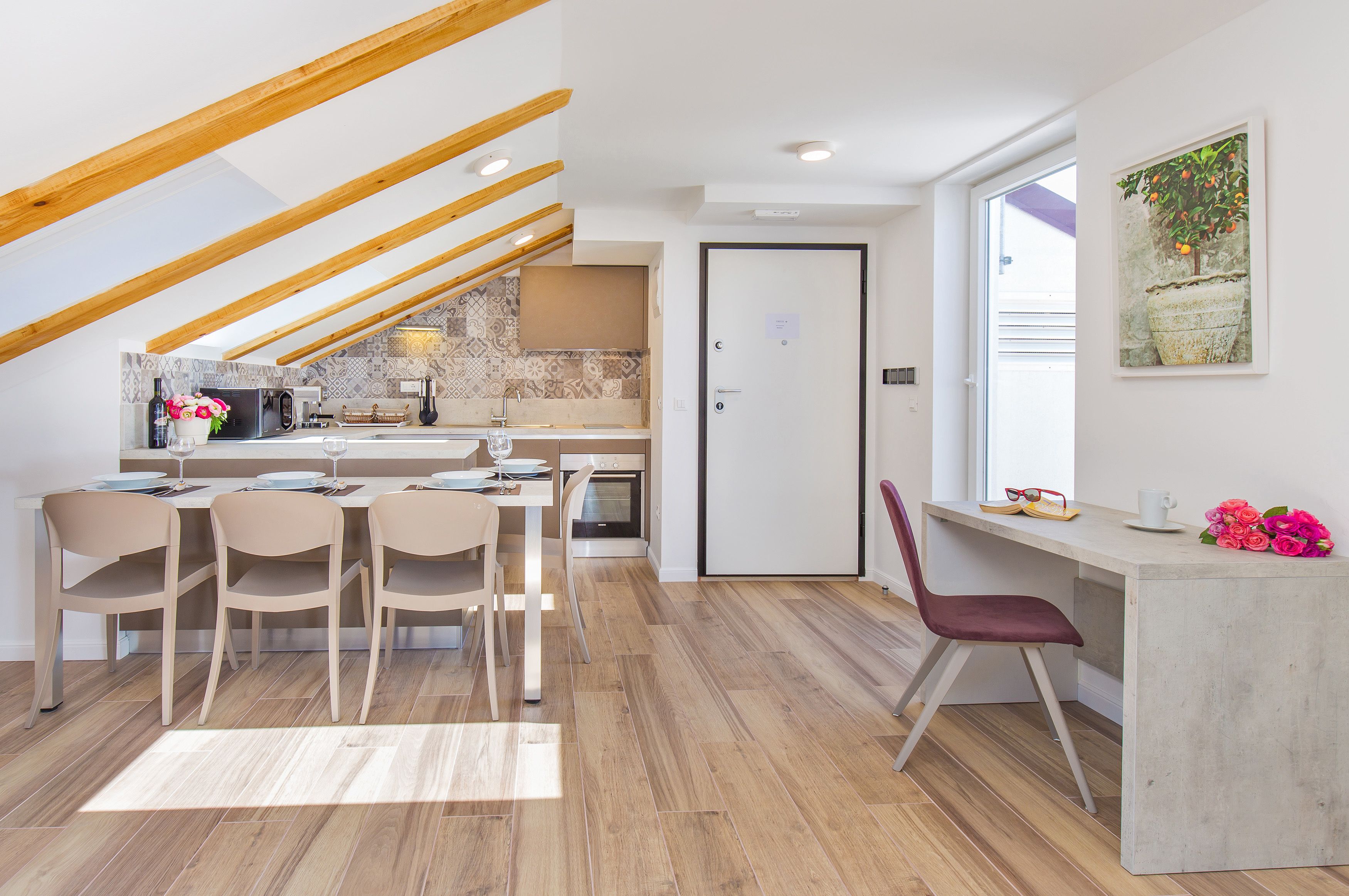 Una cocina moderna con vigas de madera, una zona de comedor con sillas y un ventanal con planta en maceta.