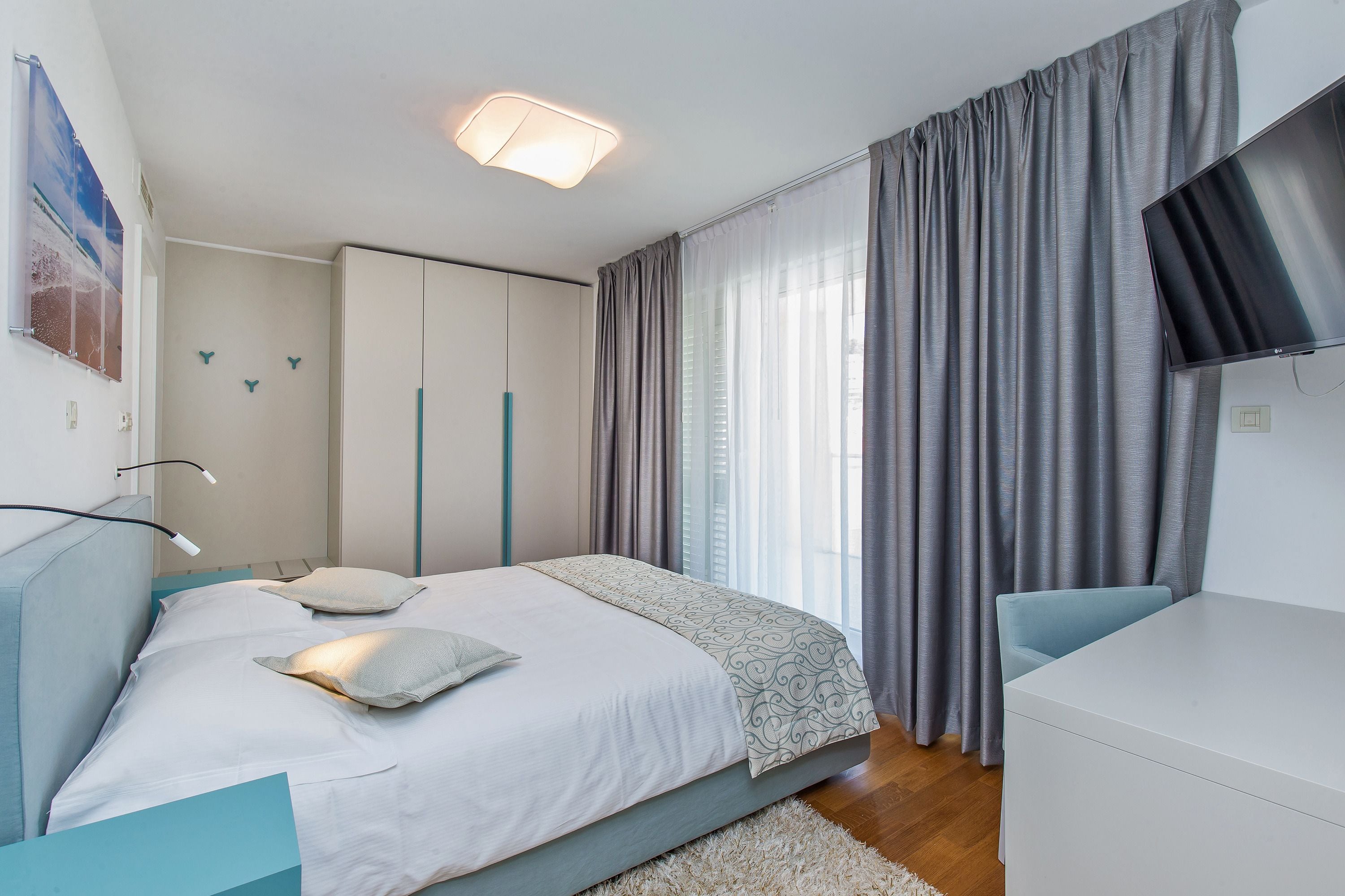 A bedroom with a bed, bedside table, TV, and curtains.