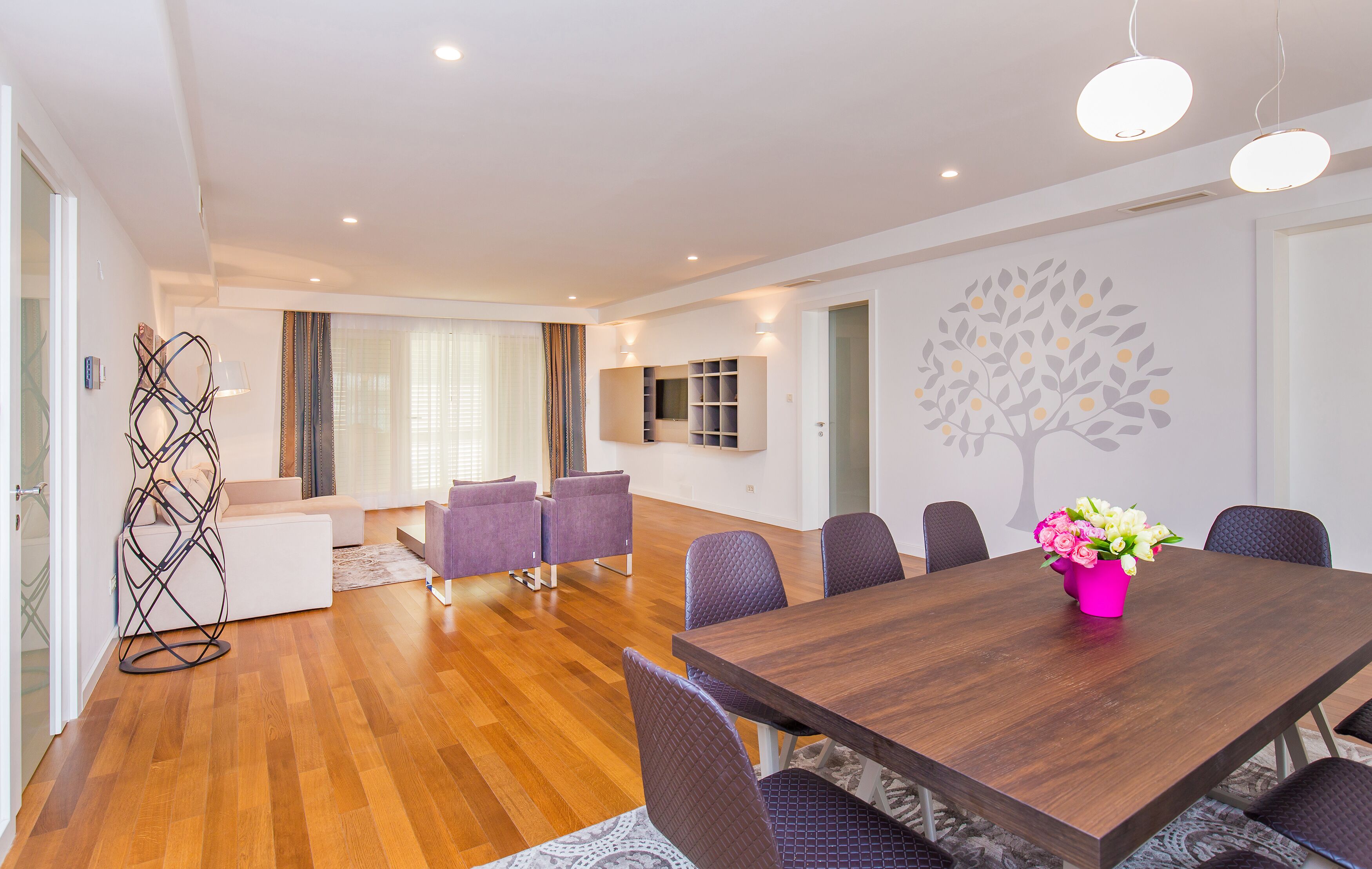 A modern dining area with a wooden table, purple chairs, and a pink vase of flowers.