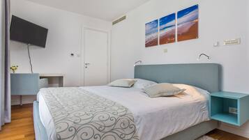 Um quarto moderno com cama, escrivaninha e TV fixada na parede.
