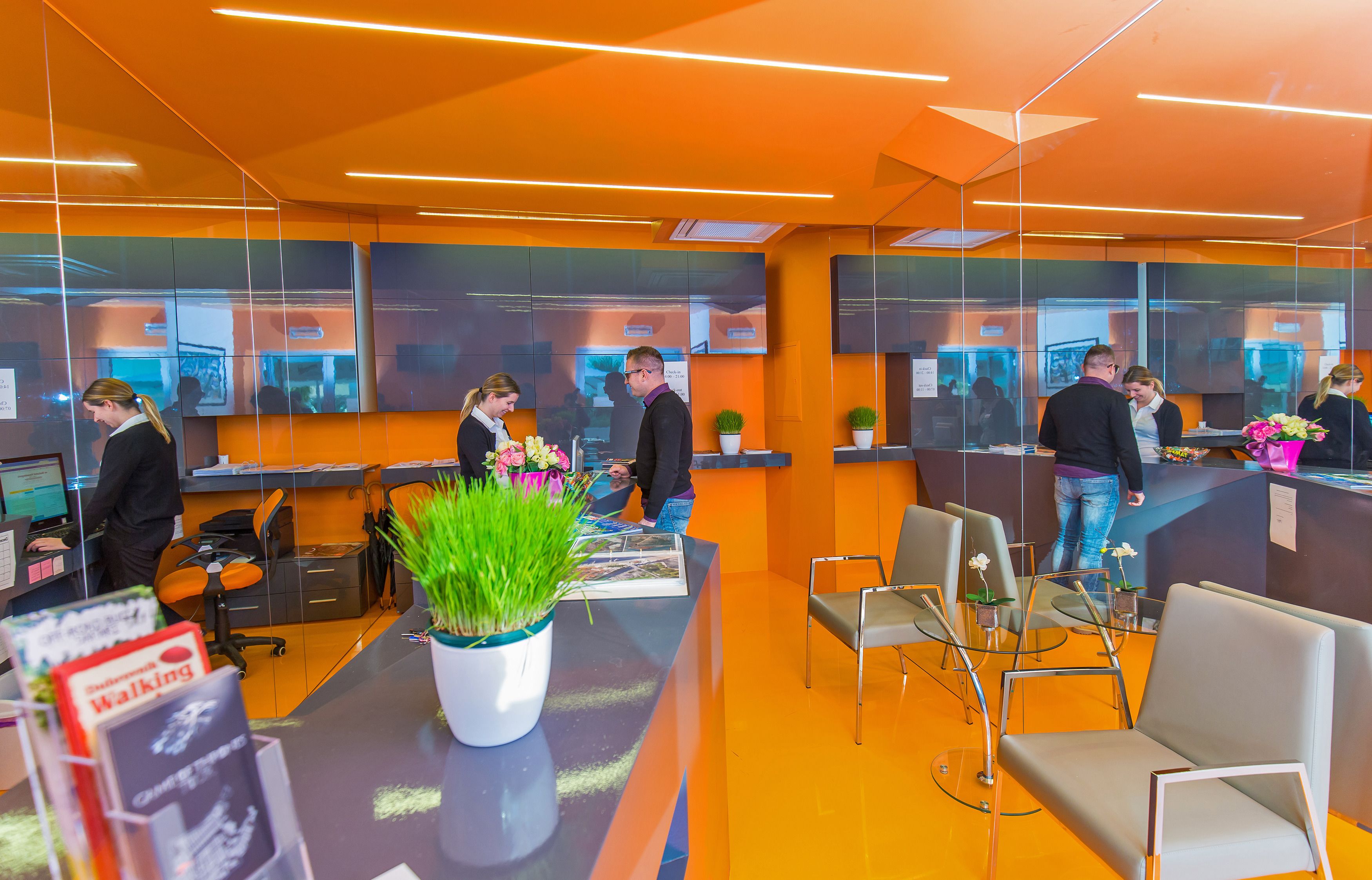 A modern reception area with glass partitions, a reception desk, and several seating areas.