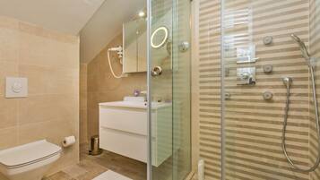 Un baño moderno con ducha de vidrio, un lavamanos blanco y un inodoro.