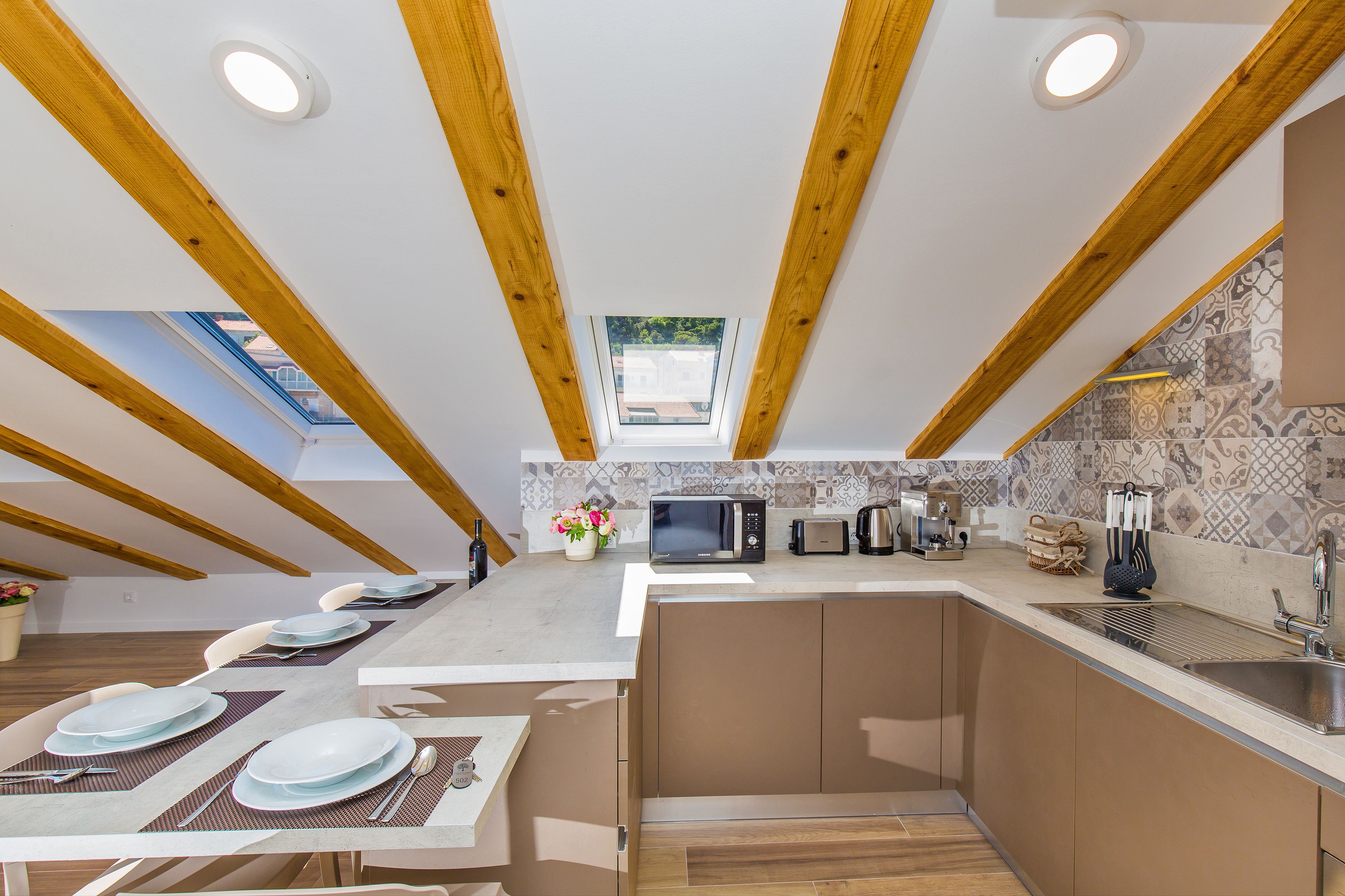 A modern kitchen with wooden beams, a skylight, and a dining area with set tables.