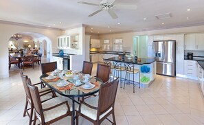 Une cuisine spacieuse équipée d’appareils électroménagers modernes, un coin repas avec une table en verre et un ventilateur de plafond.