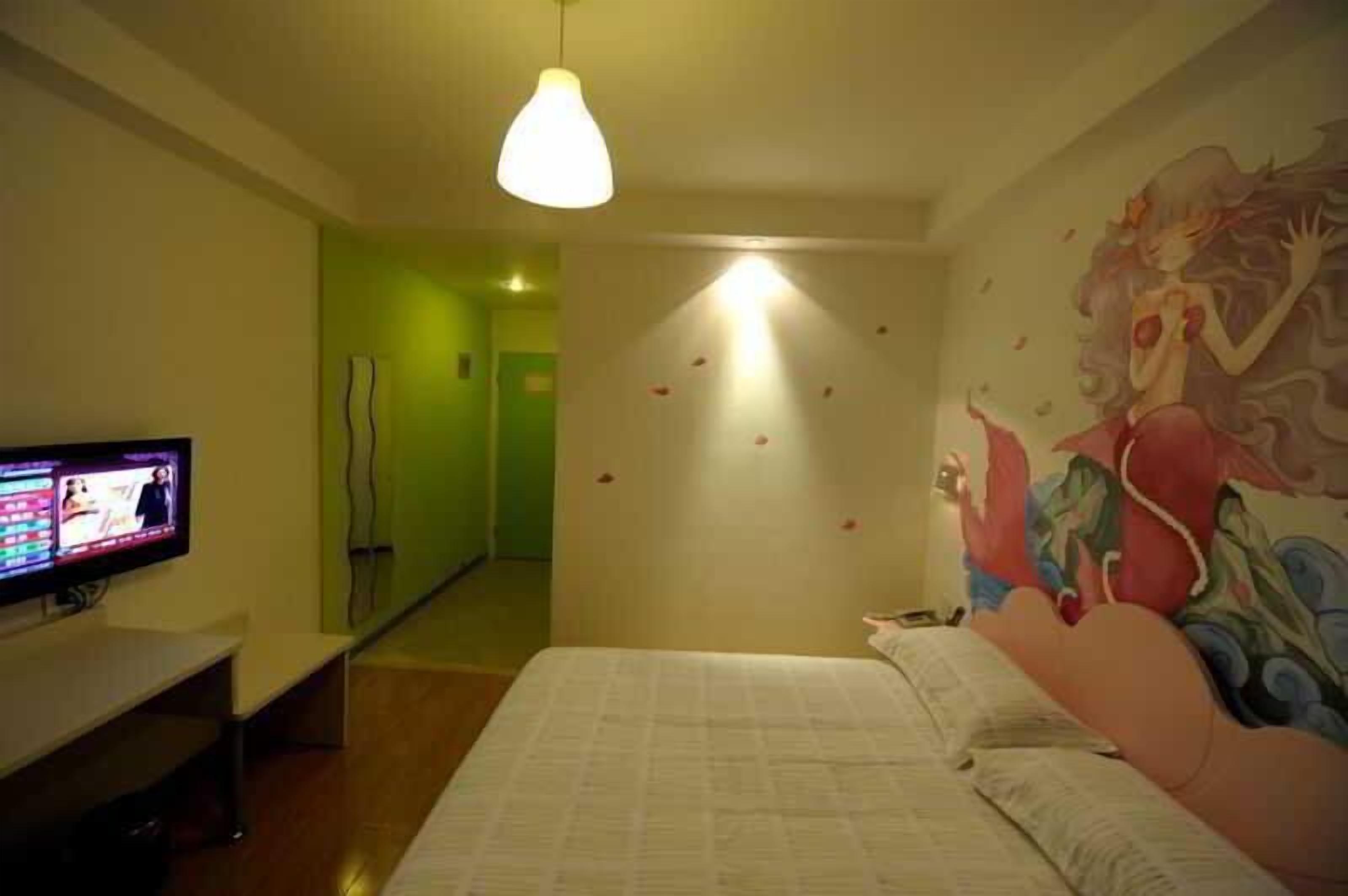 A hotel room with a bed, a television on a stand, a mirror, and a wall with a mural.