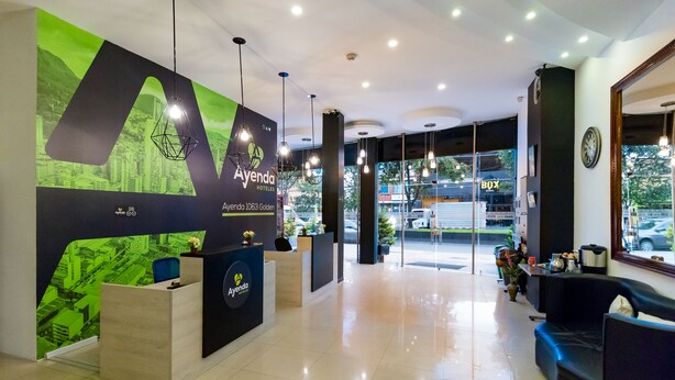 Un espace d’accueil d’hôtel au design moderne, comprenant un comptoir d’accueil, un coin salon et une vue sur la rue grâce à de grandes fenêtres.