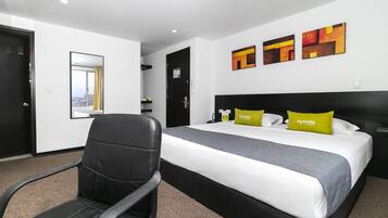 A modern hotel room with a black leather chair, a large bed with white and gray bedding, and two yellow pillows.