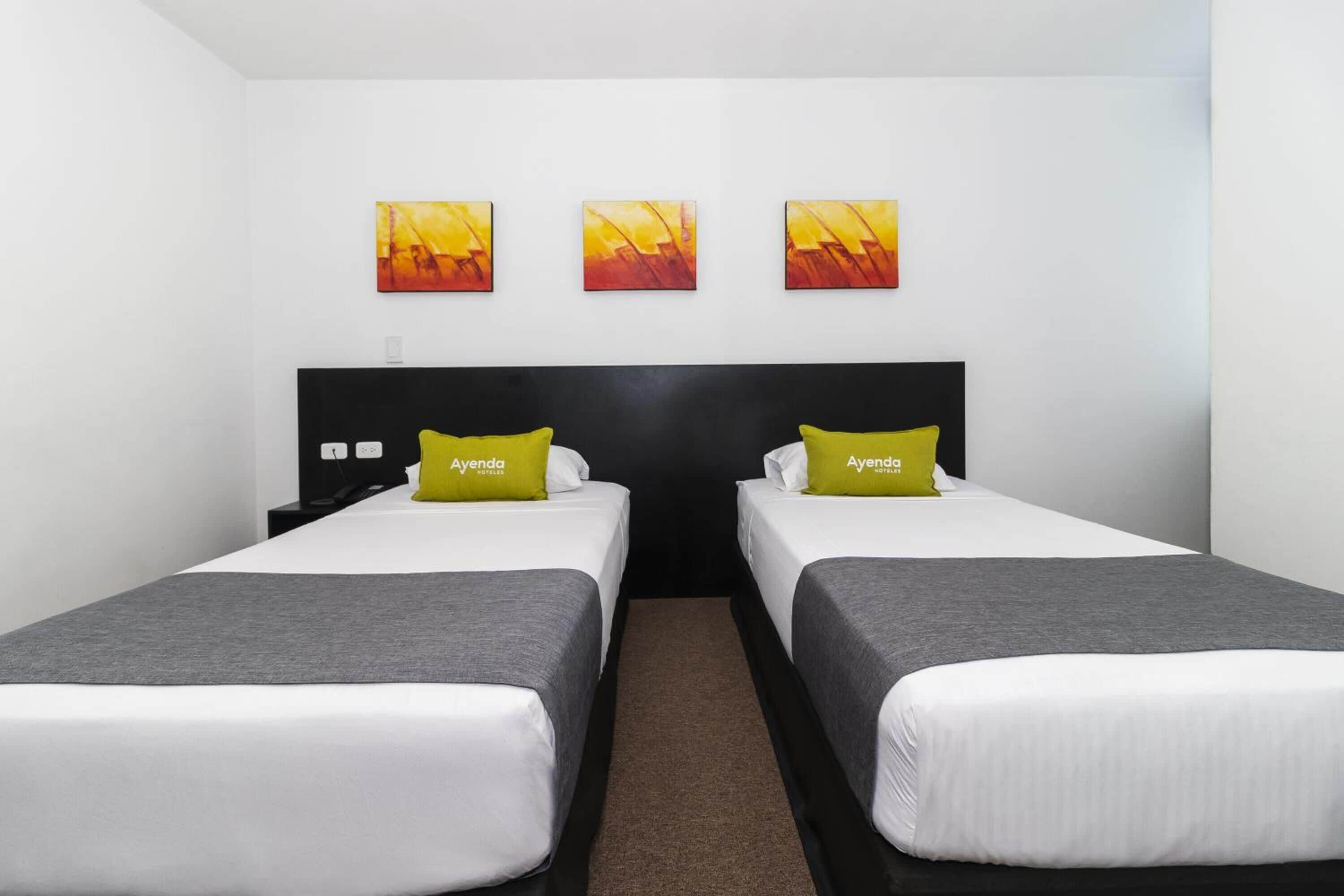 A hotel room with two beds, a black headboard, and three paintings on the wall.