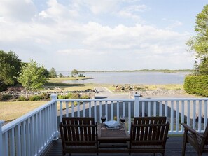 Une terrasse en bois avec deux chaises et une table, donnant sur un lac bordé d’une zone herbeuse et d’un quai.