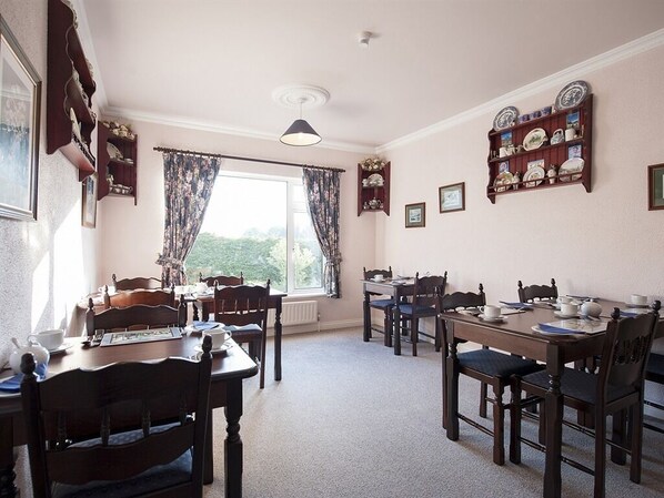 A dining room with wooden furniture, a window with curtains, and wall-mounted shelves with plates. - The Waterfront House Country Home (Oughterard)