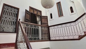 Una escalera con barandales metálicos ornamentados y un pasamanos de madera que conduce a una habitación con techo alto y tragaluz.