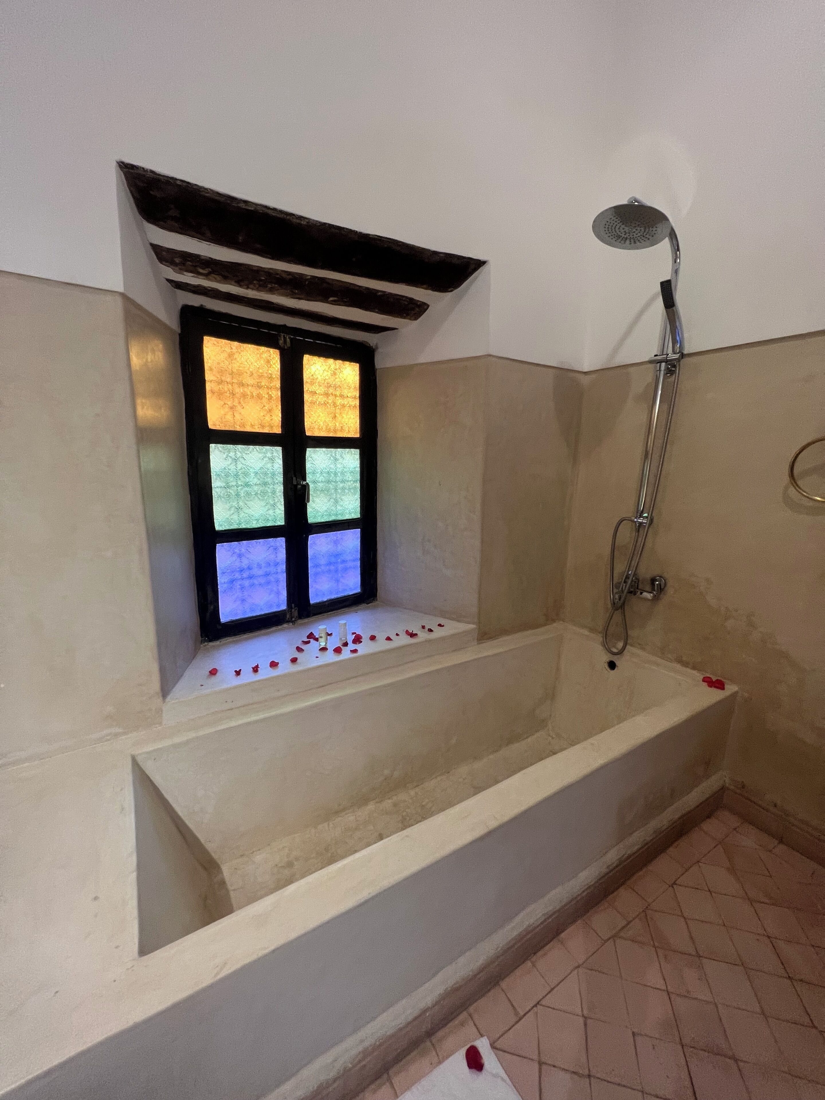 A bathtub with a window above it, a showerhead, and a tiled floor.