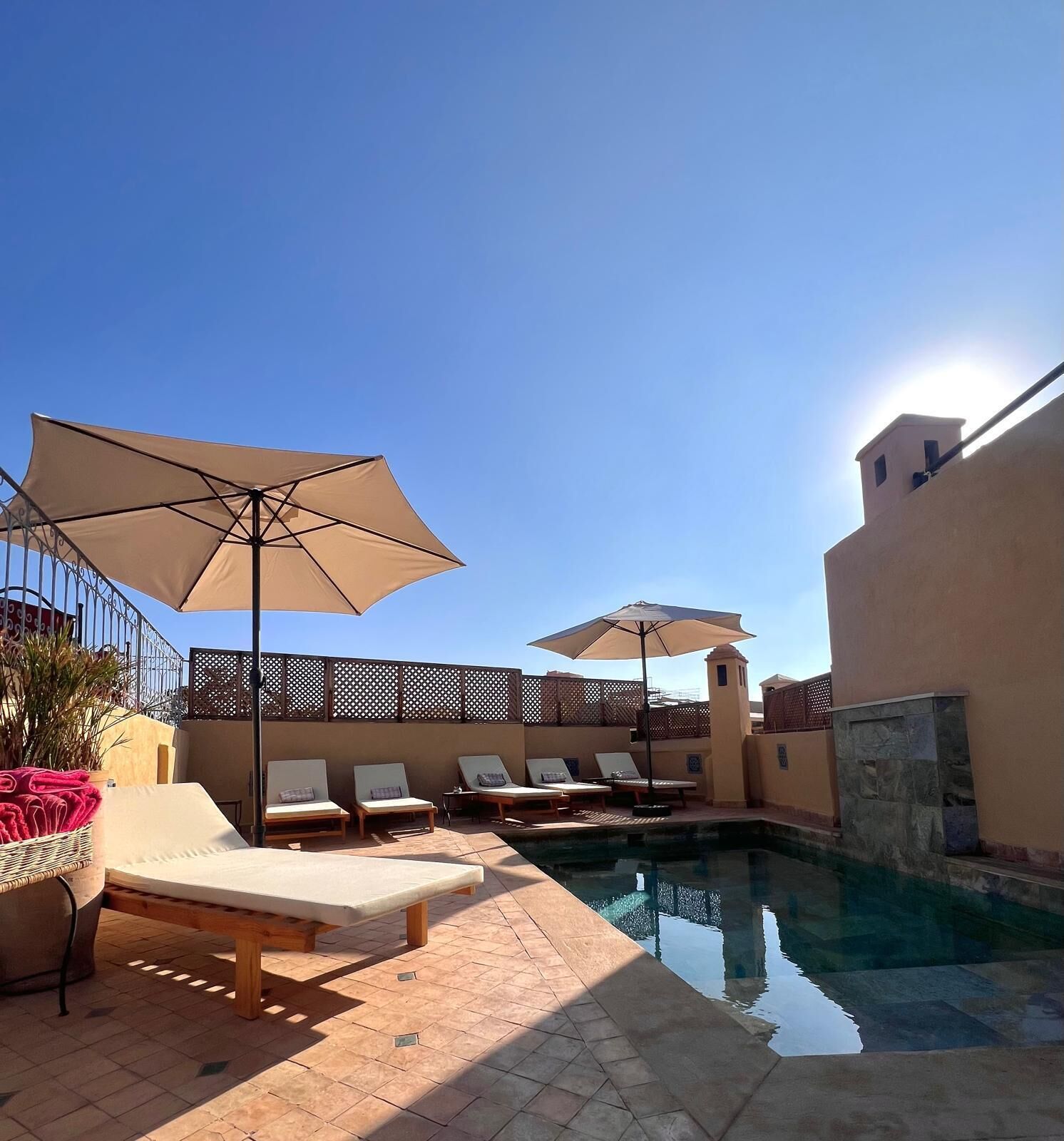Un espace aménagé au bord de la piscine, avec des chaises longues et des parasols, un ciel d’un bleu éclatant et une piscine.