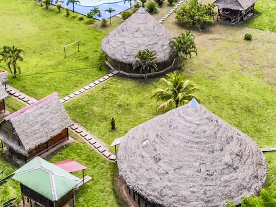 Um resort com cabanas de telhado de palha, piscina e vegetação exuberante.