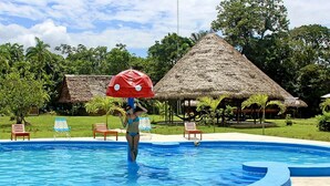 A swimming pool with lounge chairs and thatched-roof huts in the background.