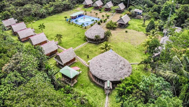 An aerial view of a resort with thatched-roof huts, a swimming pool, and lush greenery.