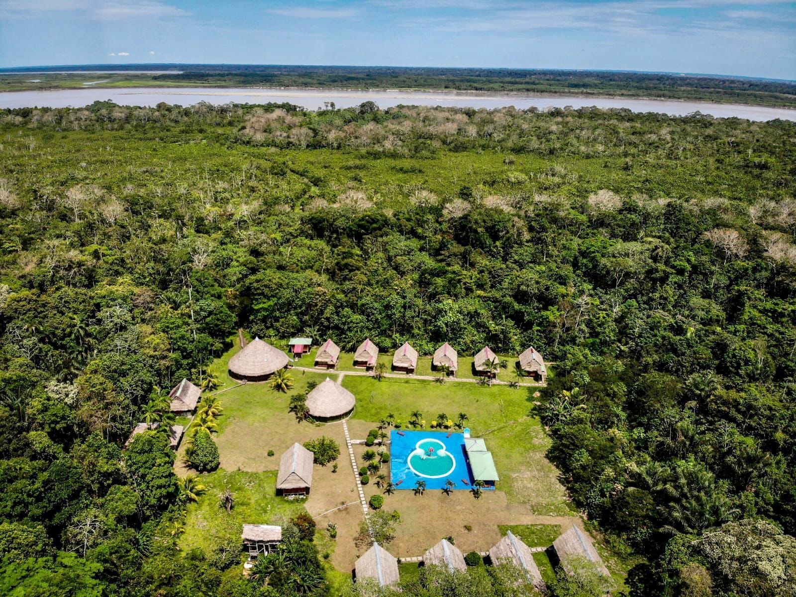 Vue aérienne d’un complexe hôtelier avec des bungalows aux toits de chaume disposés autour d’un espace piscine central.