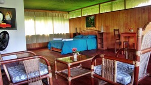 A room with a bed, a desk, and two wicker chairs.