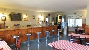 A diner with a wooden counter, bar stools, and tables with checkered tablecloths.
