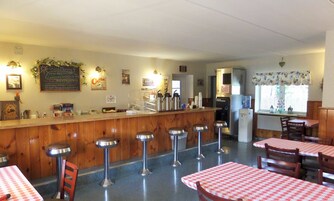 Un restaurante con mostrador de madera, taburetes de bar y mesas con manteles a cuadros.