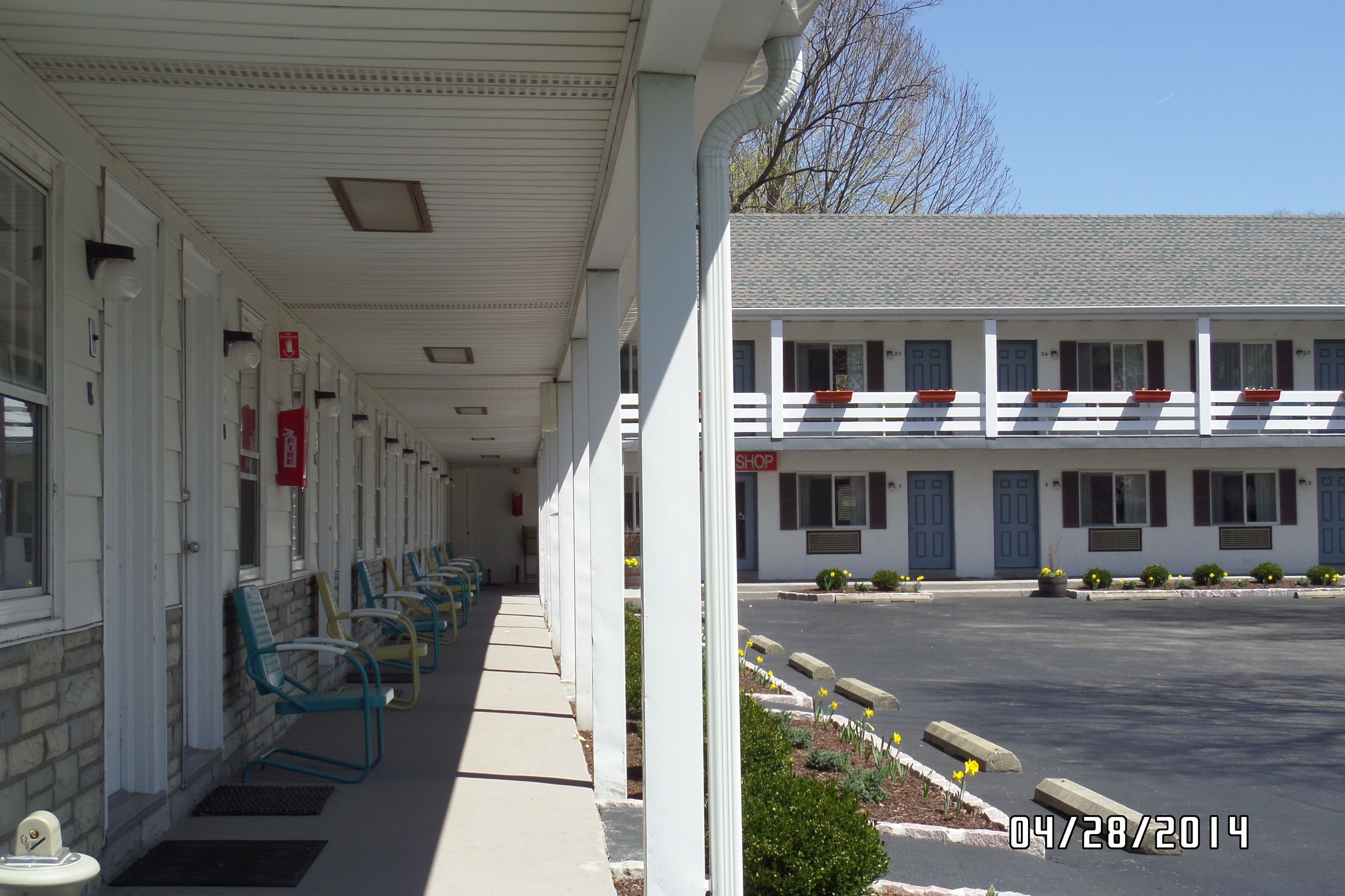 A motel with a row of rooms, outdoor seating, and a parking lot.