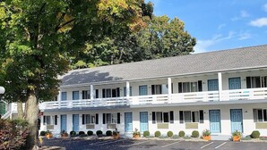 A two-story motel with a white facade, blue doors, and a parking lot in front.