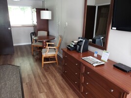 Habitación de hotel con una mesa de comedor de madera y sillas, una cafetera, un escritorio con cajones y un espejo grande.