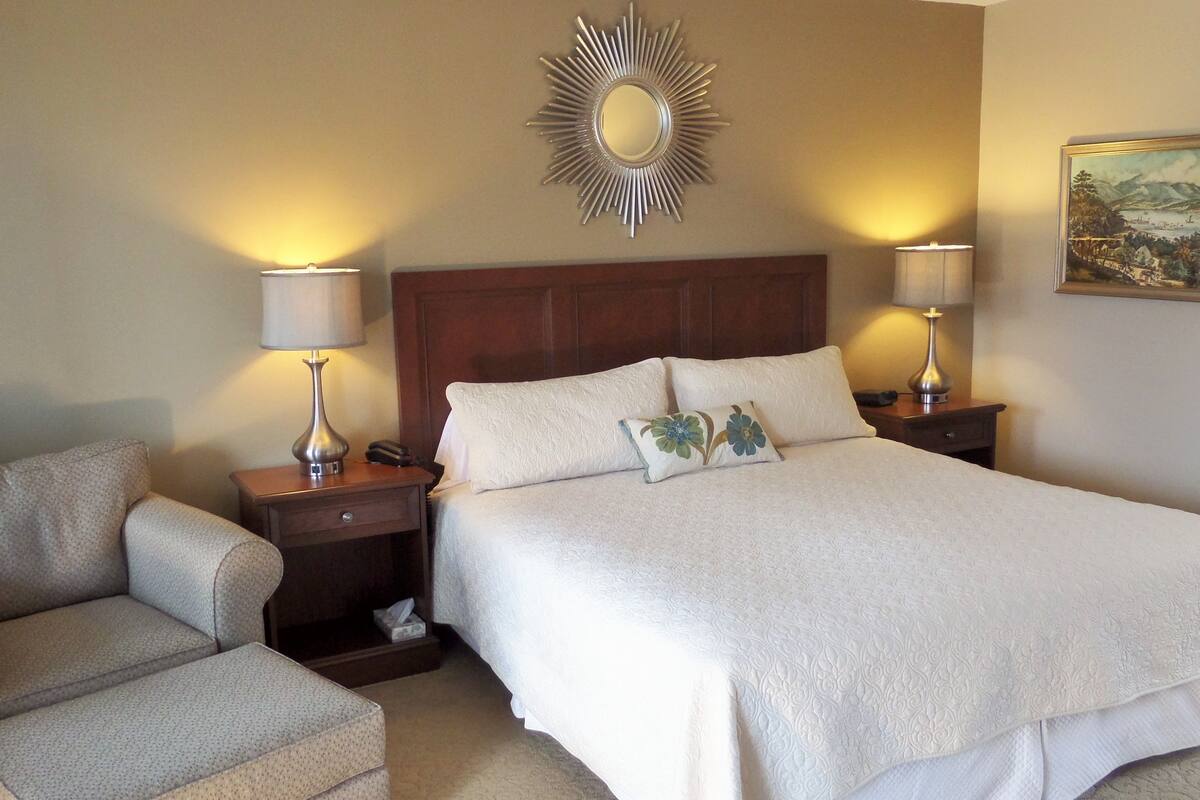 A hotel room with a large bed, two bedside tables with lamps, a wooden headboard, and a decorative mirror on the wall.